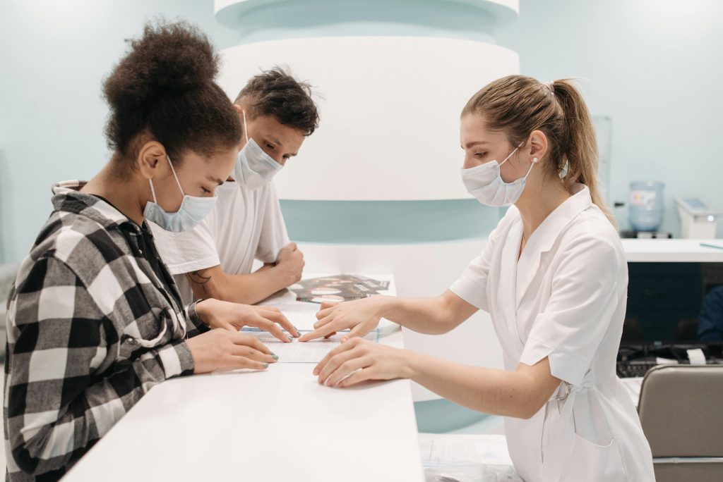 A healthcare professional in a medical setting assists patients at a clinic desk, emphasizing care and teamwork.